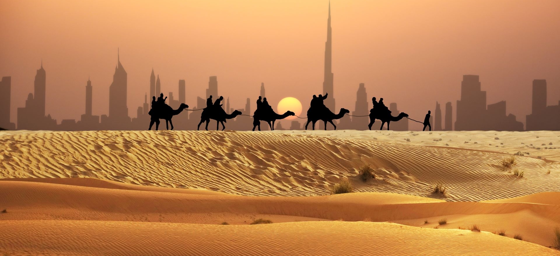 Escursione in cammelli con un gruppo di turisti sulle dune del deserto a Dubai con sfondo lo skyline